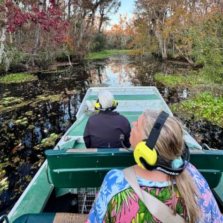 Visitors riding an airboat through the scenic waterways near DeLand, Florida, surrounded by cypress trees and lush wetlands.